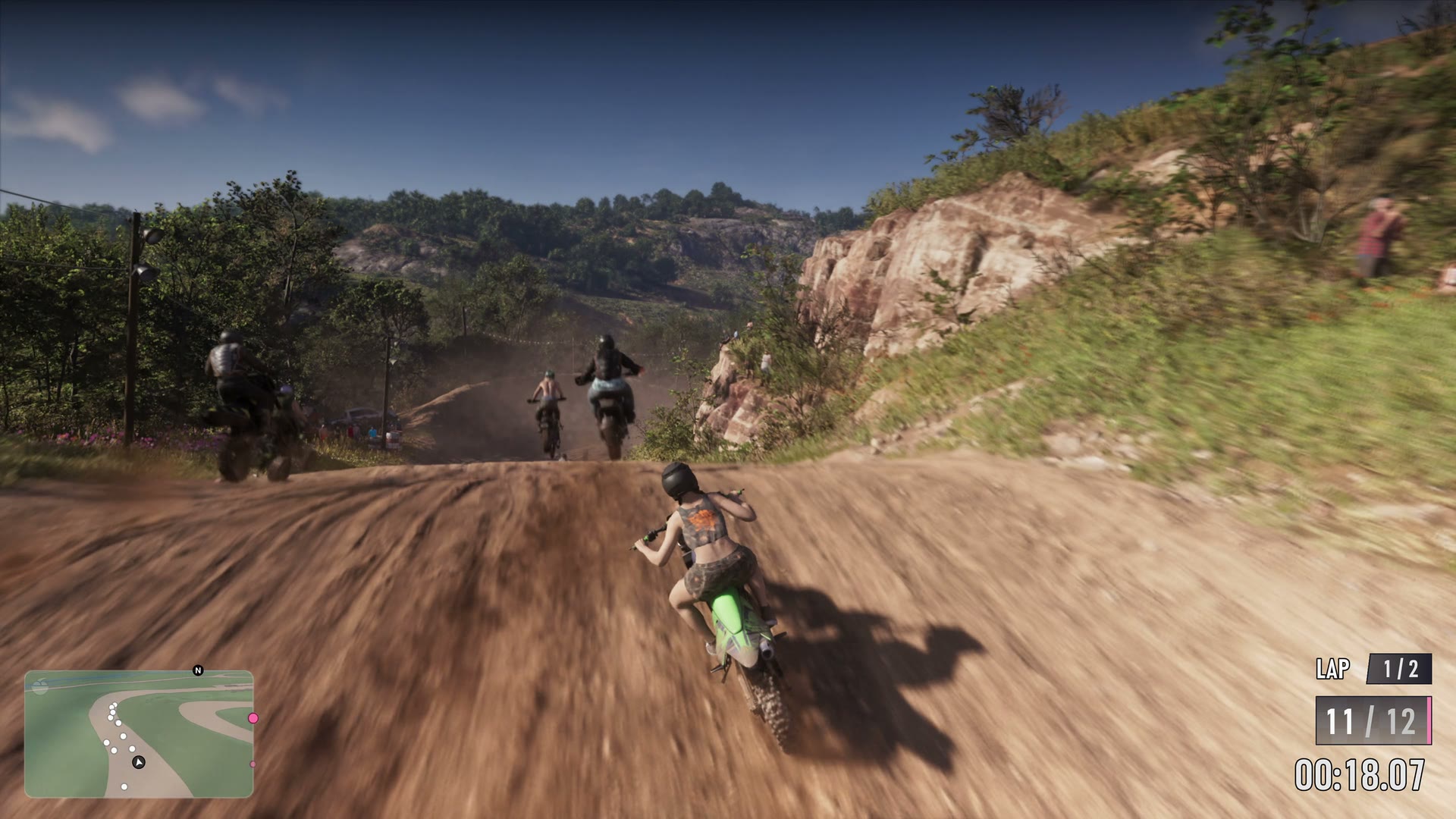 A twelve-rider motocross race on a hillside dirt track, lap 1 of 2